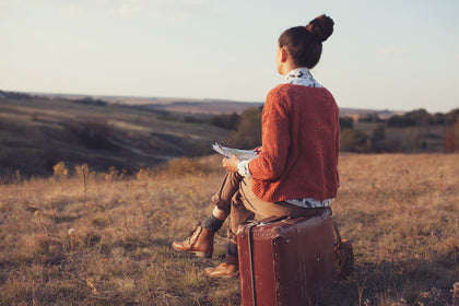 artist sitting on a luggage in a grassy field looking at a hill