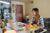 woman sitting at a desk with art supplies in front of her, she is looking at the computer.