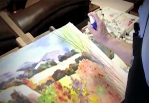 person using a spray bottle over a colorful canvas painting