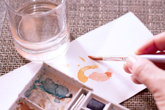 artist painting yellow watercolor on paper with watercolor brush