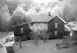 a black and white photo of a two story house surrounded with trees behind it