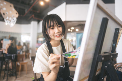 woman holding a paint palette and paintbrush painting on a canvas